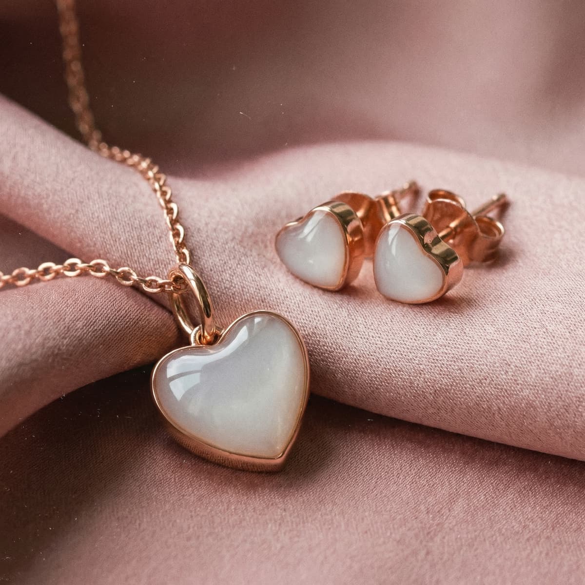 Rose gold heart-shaped breastmilk keepsake necklace with matching heart stud earrings on soft fabric, a sentimental 1 year breastfeeding gift for moms