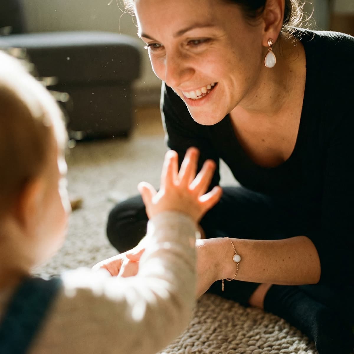 Smiling mom playing with her baby on the floor, wearing elegant white keepsake earrings and matching bracelet as a meaningful 1 year breastfeeding gift to celebrate motherhood.