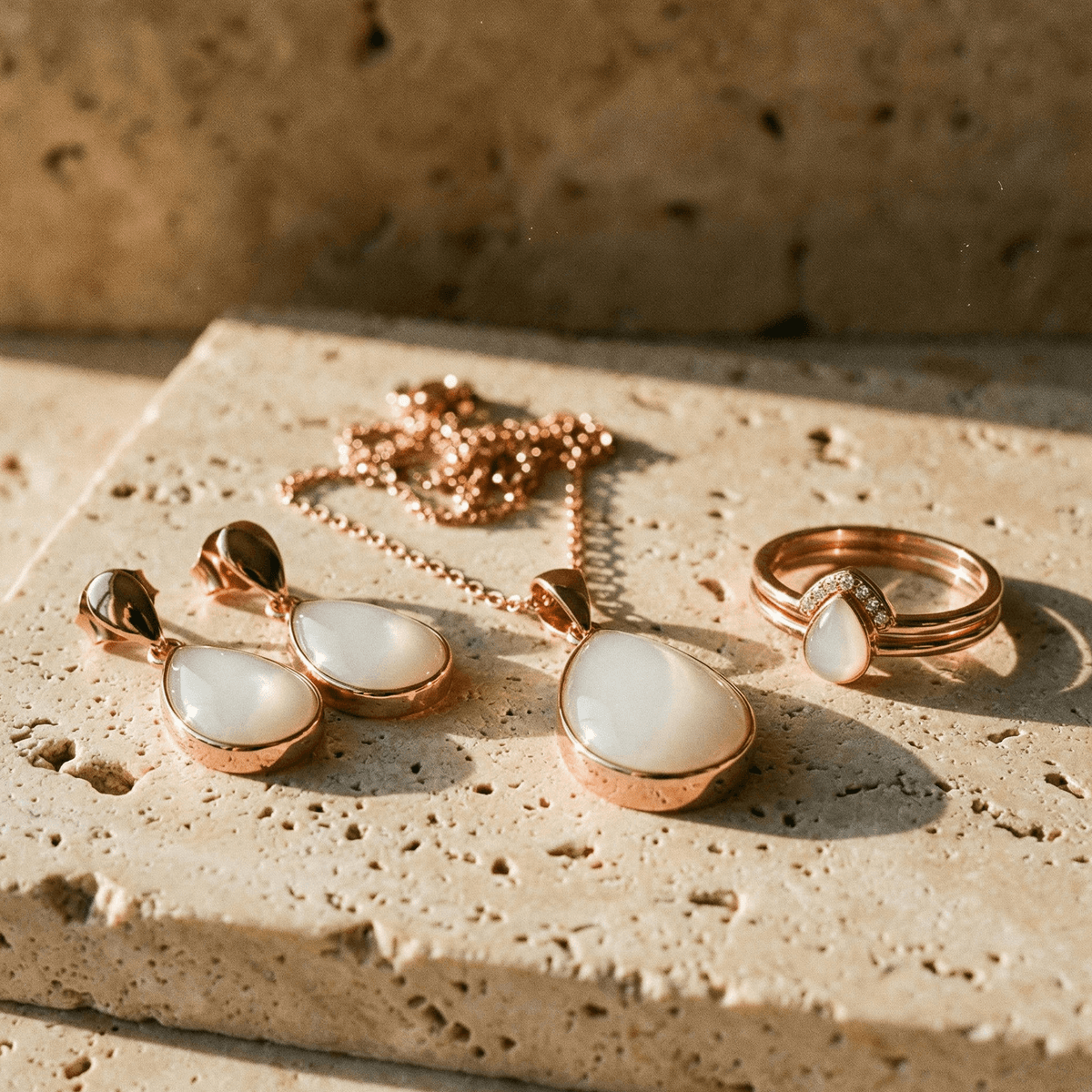 Rose gold breastmilk keepsake jewelry set featuring a teardrop pendant necklace, matching earrings, and a ring with milky white resin stones, a thoughtful 6 months breastfeeding award gift displayed on a sunlit stone surface.