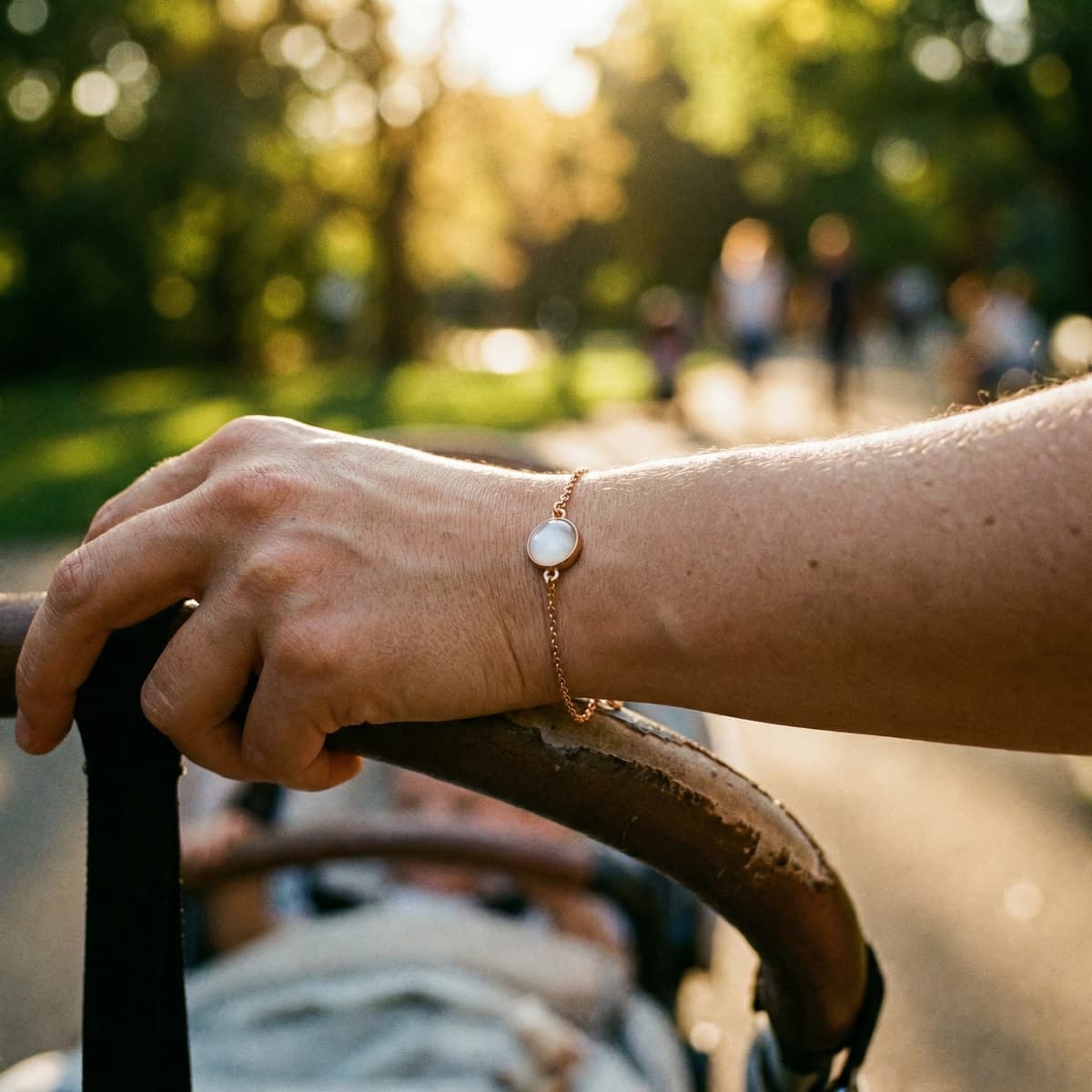 Mom pushing a stroller outdoors in warm sunlight, wearing a delicate gold bracelet with a milky white resin stone baby keepsake for mom