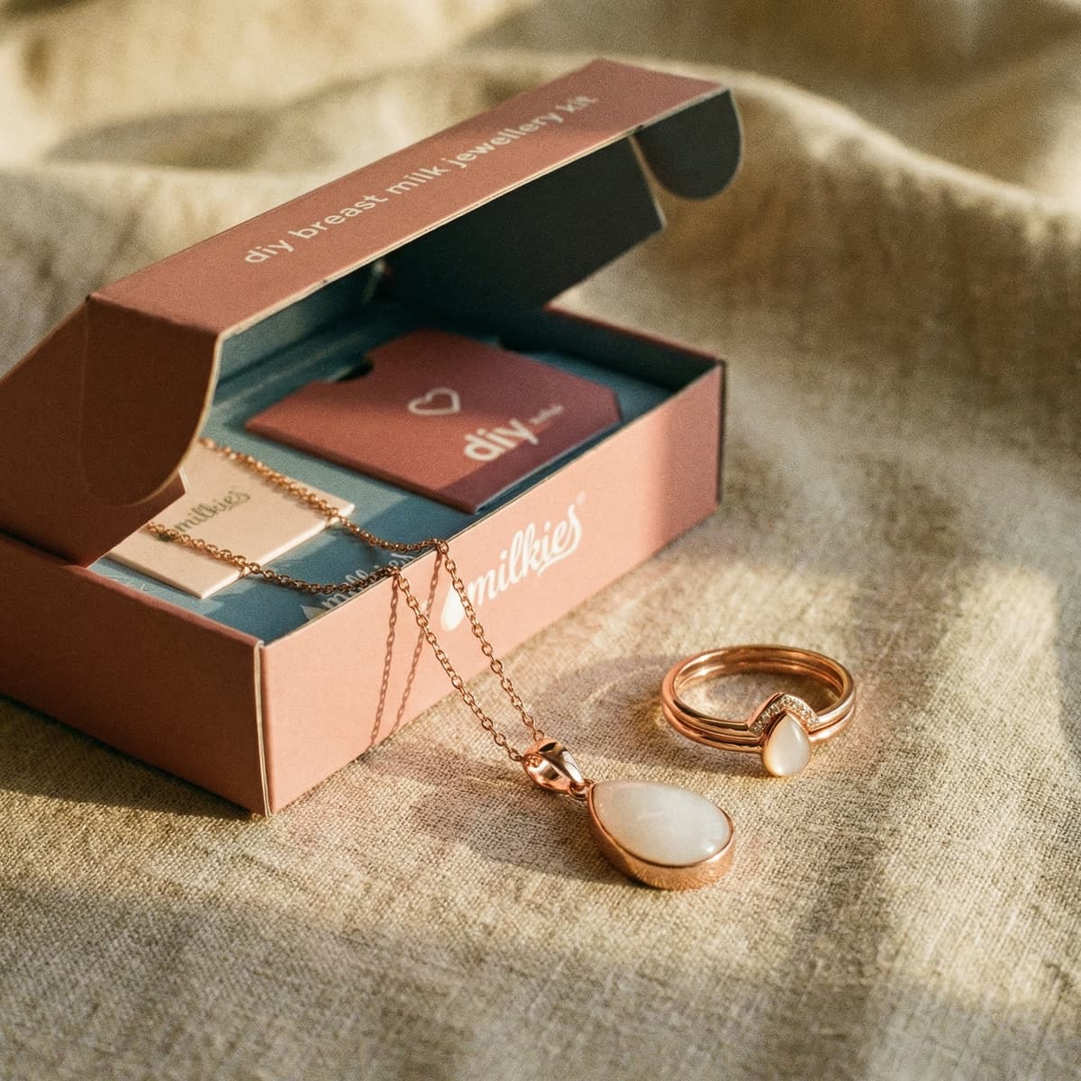 Elegant DIY by MILKIES breastmilk jewelry kit box featuring rose-gold teardrop necklace and matching ring on linen, highlighting one of the best push presents for new moms.