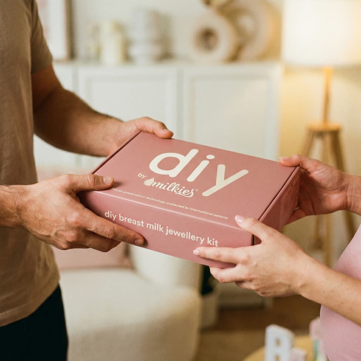 Hands holding a DIY by MILKIES breast milk jewellery kit box, a thoughtful breastfeeding gift for creating a keepsake at home.
