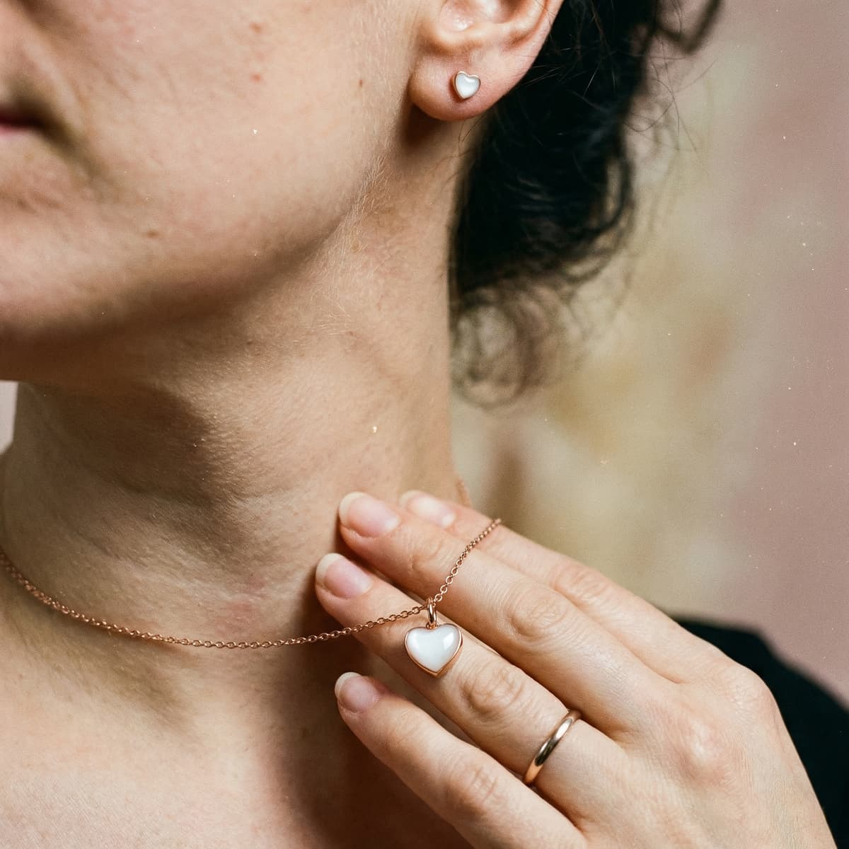 Close-up of a woman wearing a rose-gold heart pendant necklace and matching heart stud earrings, a sentimental keepsake piece ideal as a breastfeeding journey gift.