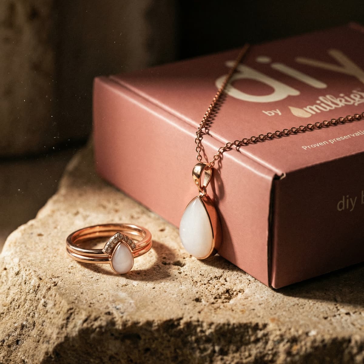 Rose gold breastmilk keepsake necklace and ring with teardrop white stones next to a pink DIY by MILKIES kit box, a meaningful breastfeeding journey gift.