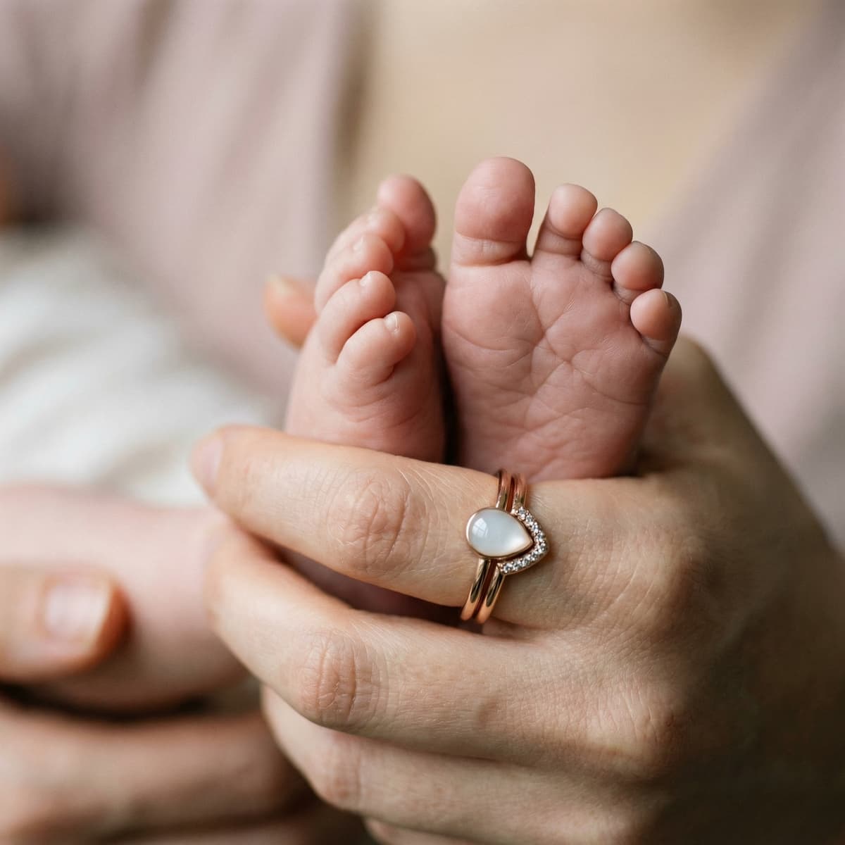 Mother holding a newborn’s tiny feet while wearing a rose-gold ring with a milky white stone, a breastfeeding keepsake jewelry piece.