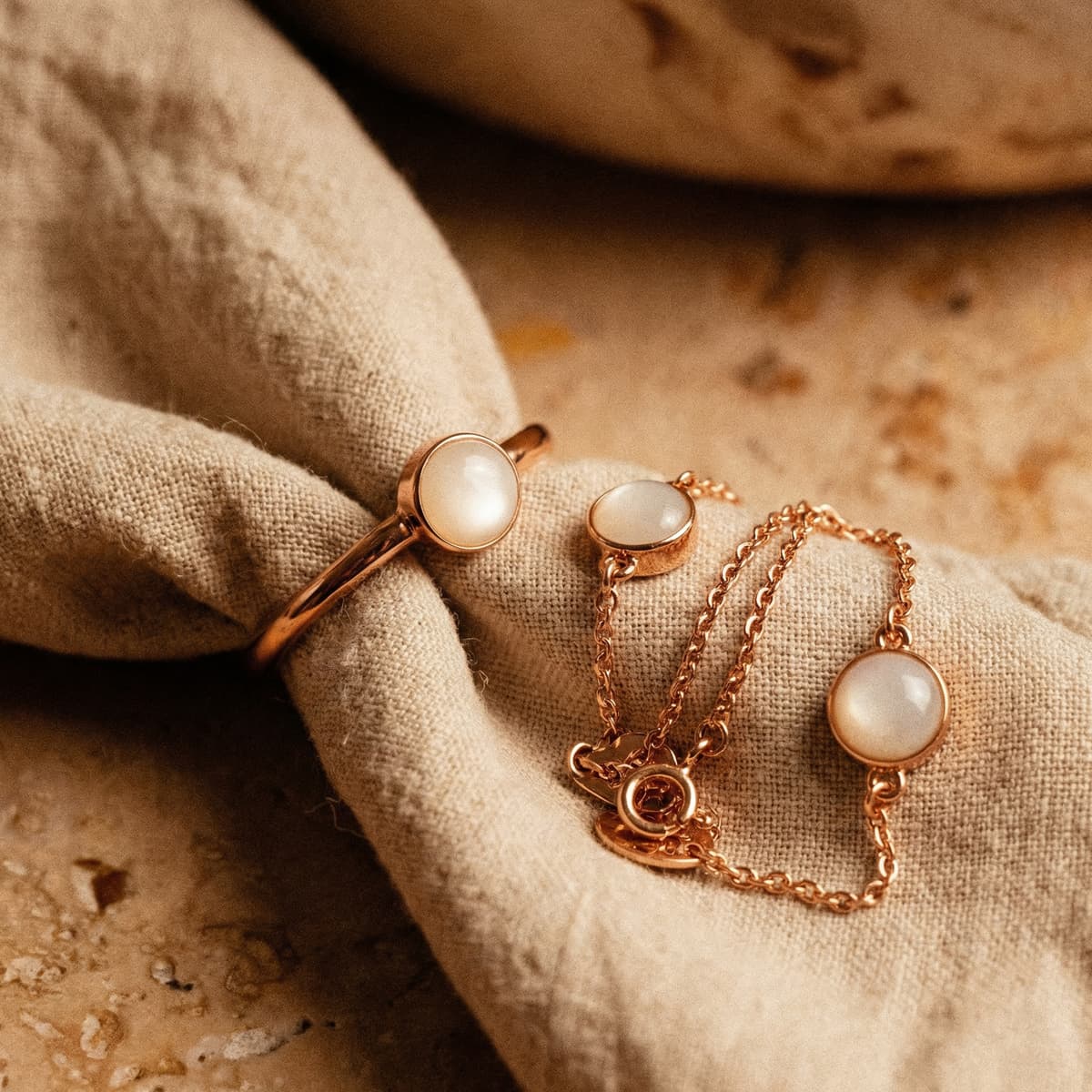 Rose gold jewelry set with a milky white resin stone breastmilk bracelet, matching ring, and stud earrings displayed on soft beige fabric