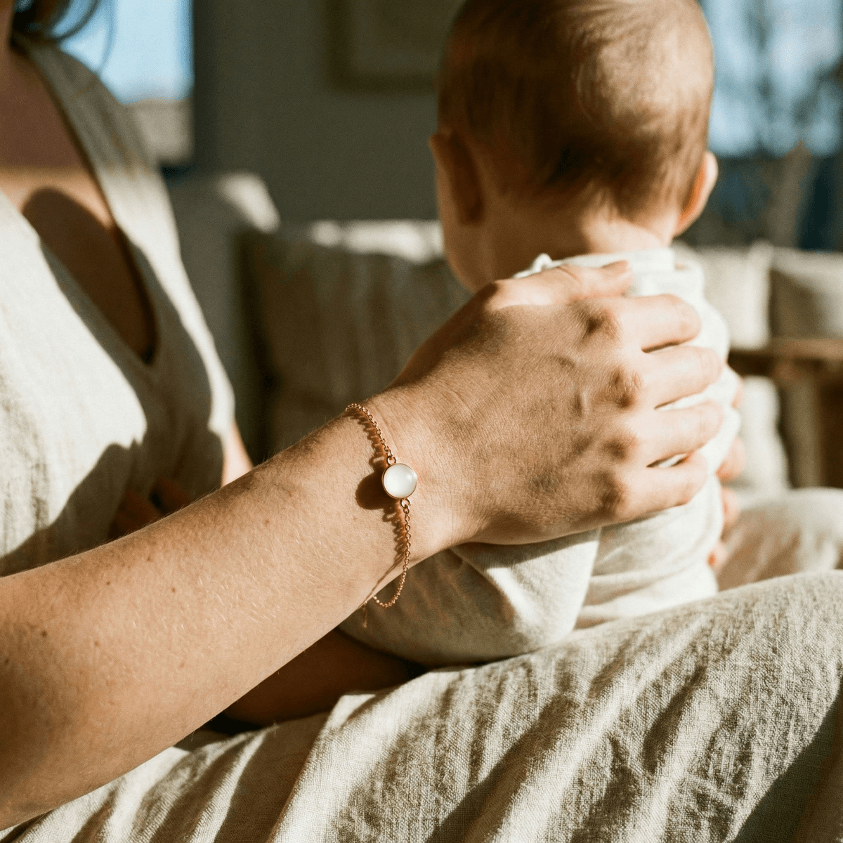 A mother cuddles her baby in warm light while wearing a delicate keepsake bracelet, showing why a breastmilk bracelet diy kit is a meaningful way to create a personal breastmilk jewelry memory at home.