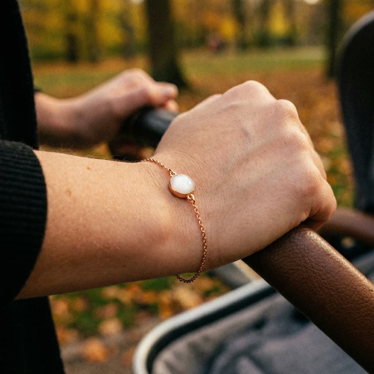 Rose gold keepsake bracelet with a milky-white resin charm made from an at-home breastmilk bracelet kit, worn by a mother pushing a stroller outdoors.