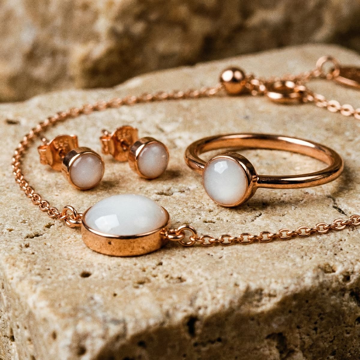 Rose gold jewelry set with a milky white resin stone—bracelet, ring, and matching stud earrings—showing results made using a breastmilk bracelet kit on a textured stone background.