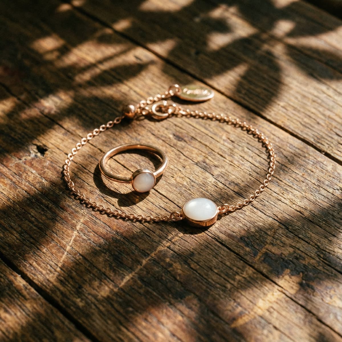 Gold chain jewelry set on rustic wooden boards in warm sunlight, featuring a ring and delicate breastmilk bracelets with smooth white resin stones.