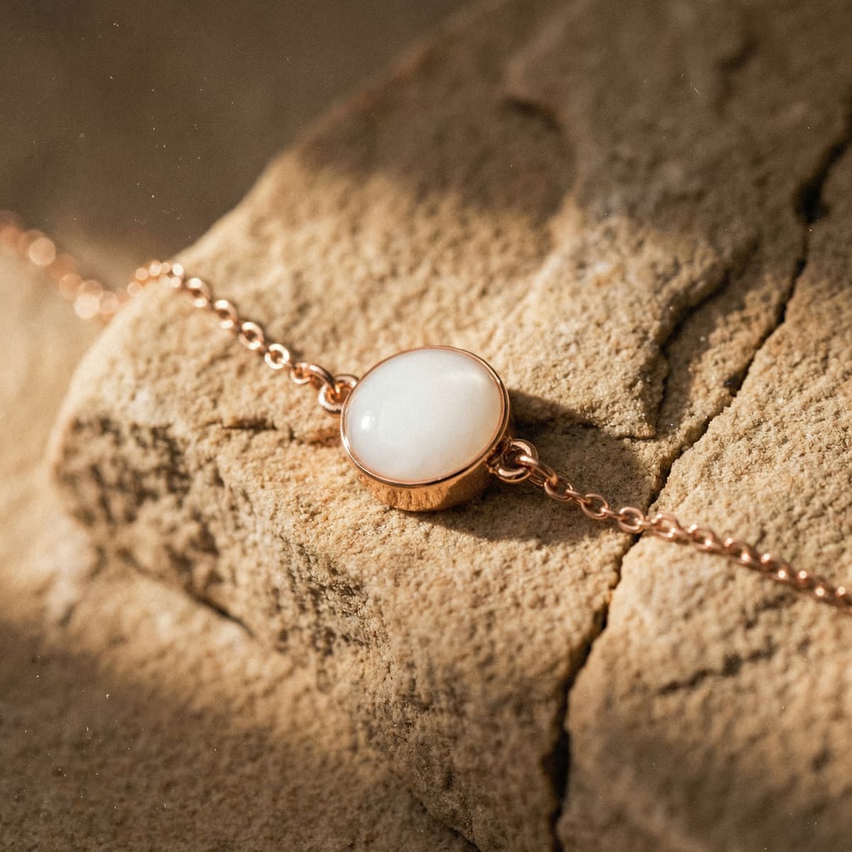 Rose-gold chain bracelet with a milky white resin charm on a textured stone surface, showcasing elegant breastmilk bracelets as handcrafted keepsake jewelry.