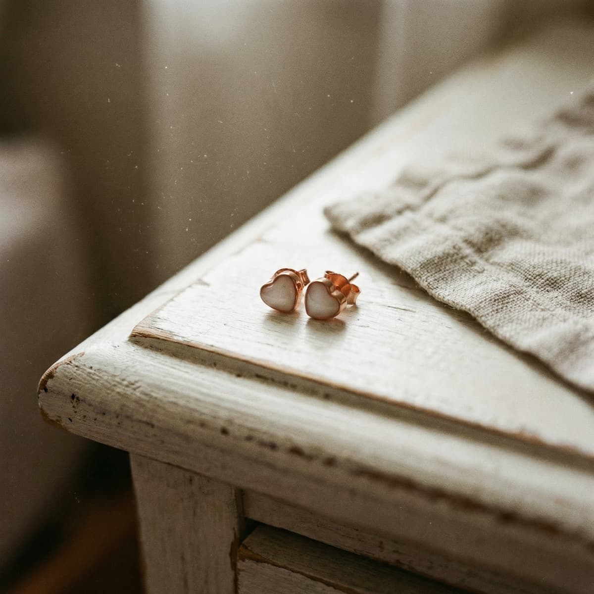 Heart-shaped rose gold stud earrings with milky white resin stones on a rustic wooden table, showcasing a finished keepsake made with a breastmilk earring diy kit.