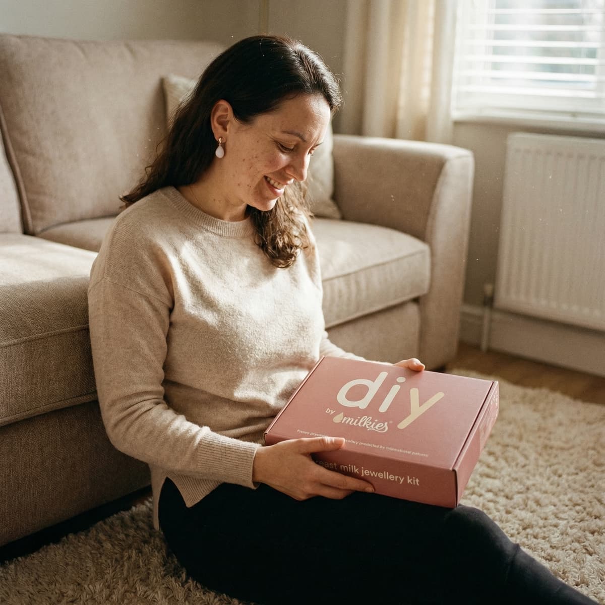 Smiling mom at home holding a DIY by MILKIES keepsake box, showing why a breastmilk earring diy kit is an easy, private way to create breast milk jewelry yourself.
