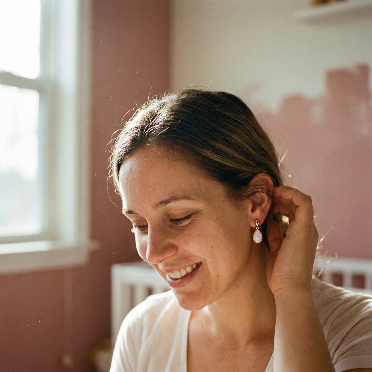Smiling mother in warm indoor light wearing a teardrop keepsake earring, showing why a breastmilk earring making kit is a meaningful DIY way to create a personal breastmilk jewelry memento at home.