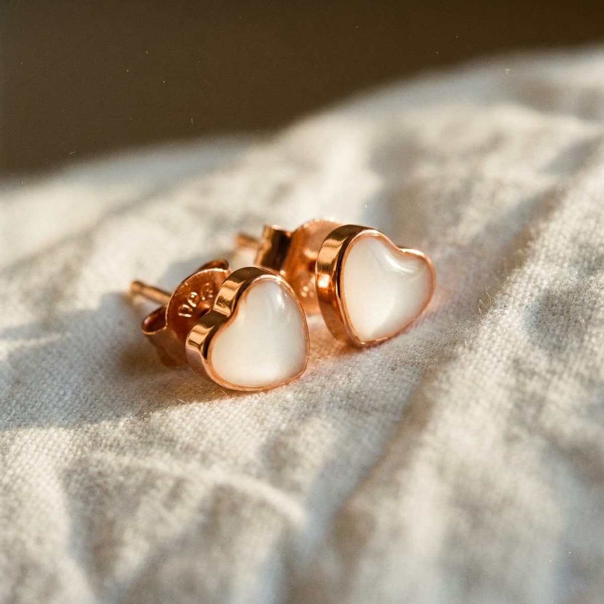 Close-up of heart-shaped breastmilk keepsake stud earrings in a rose gold setting, made using a breastmilk earrings diy kit, resting on soft fabric in warm natural light.