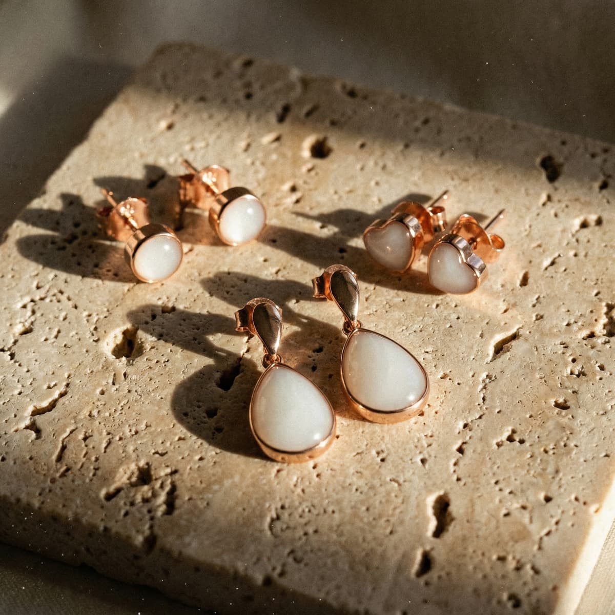 Rose gold-plated studs with milky white resin stones and teardrop and heart earrings displayed on a textured stone slab, featuring a DIY breastmilk earrings kit
