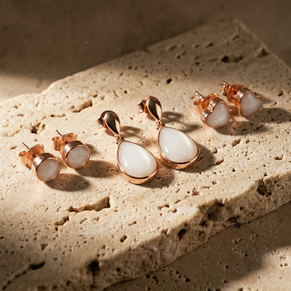Rose-gold and milky white teardrop, heart, and round stud earrings on a stone surface, showing finished keepsakes made with a breastmilk earrings making kit for DIY resin jewelry.