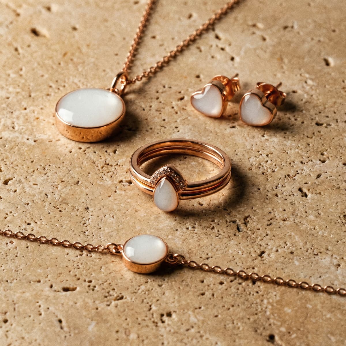Rose gold keepsake set on a neutral stone background, showing a necklace pendant, heart stud earrings, teardrop ring, and matching bracelet with milky white resin stones made using a breastmilk jewelry making kit.