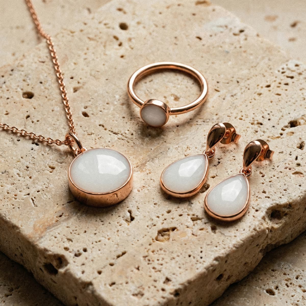 Rose gold breastmilk keepsake jewelry set showing results from a breastmilk jewelry resin kit, featuring a necklace pendant, ring, and teardrop earrings with milky white resin stones on a neutral stone surface.