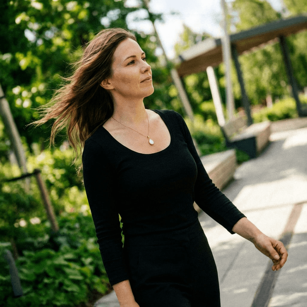 Outdoor close-up of a woman wearing one of the breastmilk necklaces, a delicate pendant keepsake on a gold chain over a black top