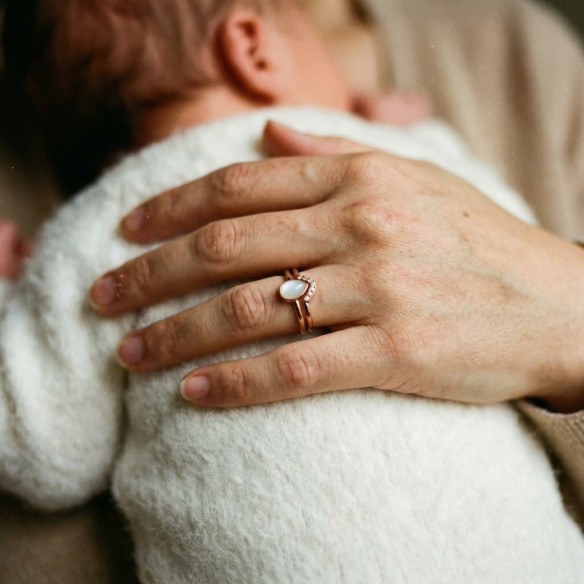 Mother cuddling her newborn while wearing a breastmilk ring with an opal-like keepsake stone, showing why an at-home DIY by MILKIES kit is a meaningful way to preserve the breastfeeding journey in a private, hands-on way.
