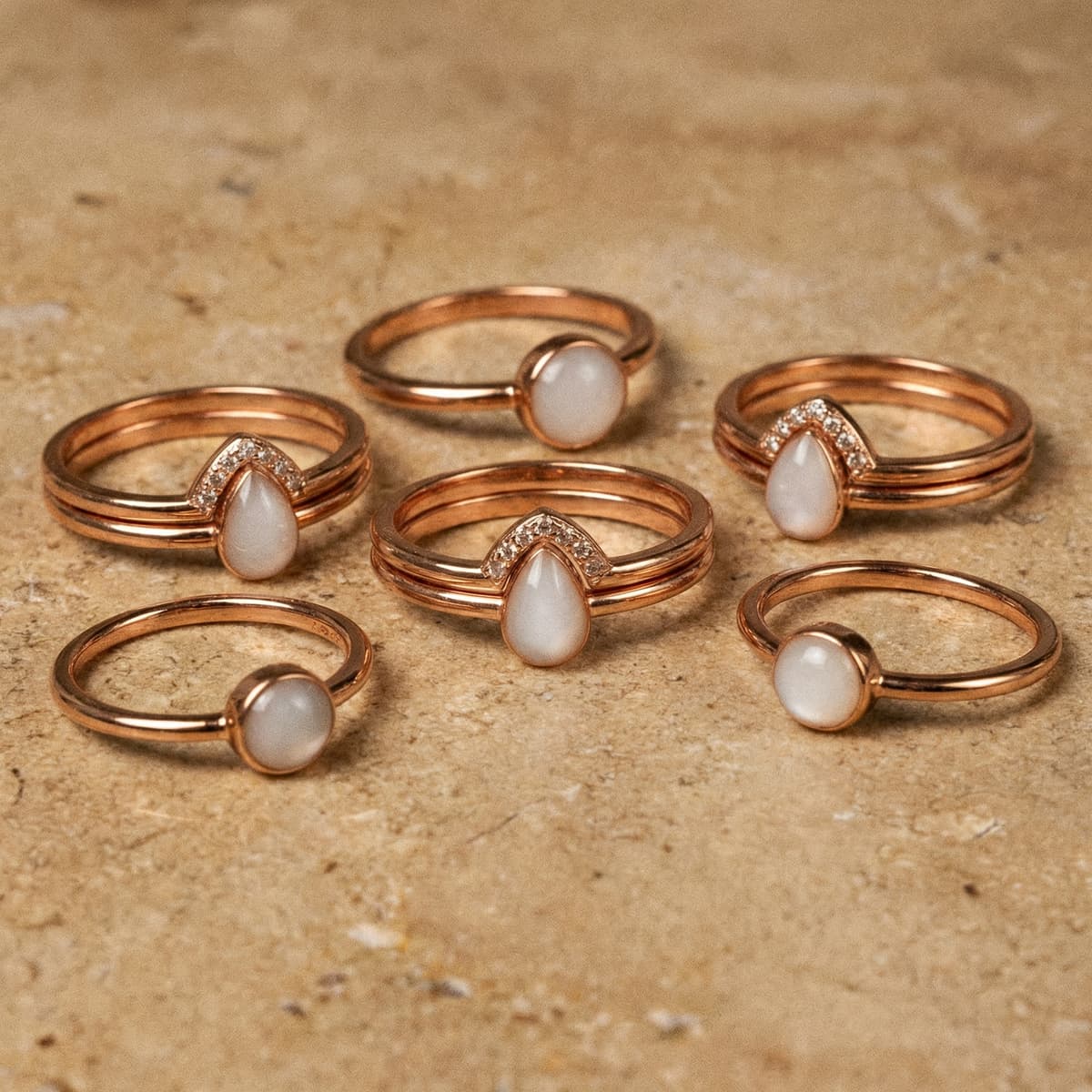 Rose-gold stacking rings with milky white breastmilk stones, finished keepsakes made using a breastmilk ring making kit on a textured beige background.