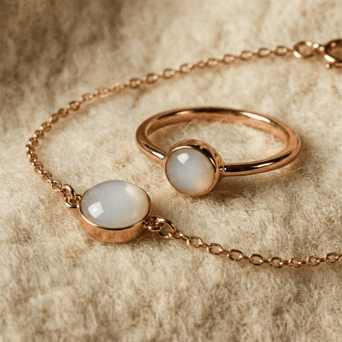 Rose gold breastmilk rings with milky white resin stones, displayed alongside a matching bracelet on soft beige fabric background