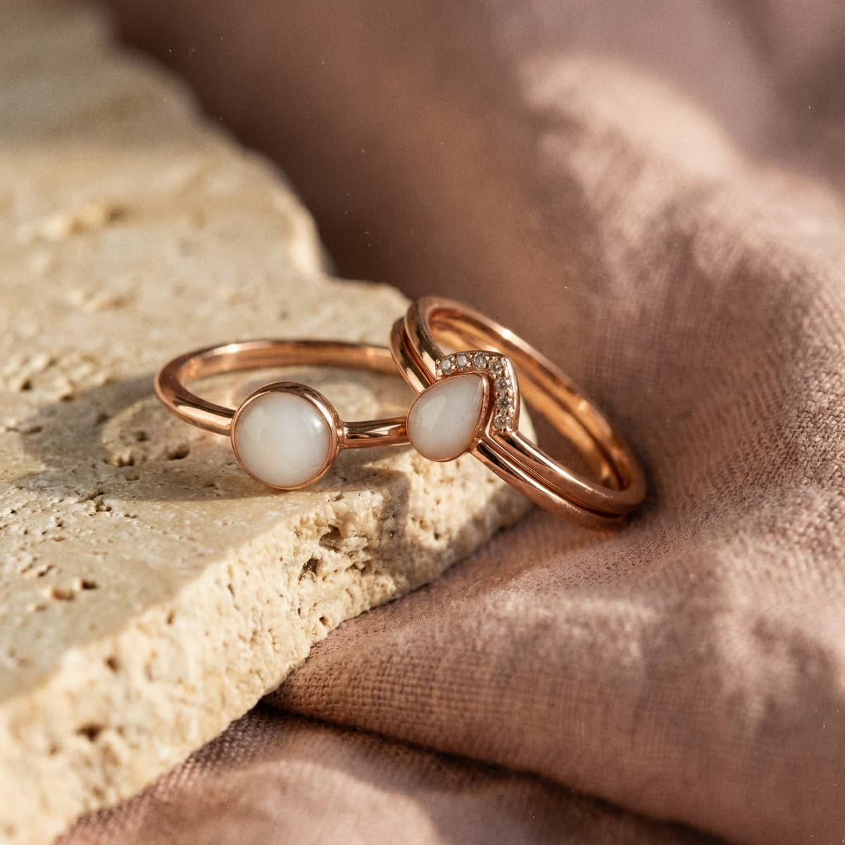 Two rose gold keepsake rings with milky white resin stones, elegant breastmilk rings displayed on natural stone and soft fabric as sentimental mother’s jewelry mementos.
