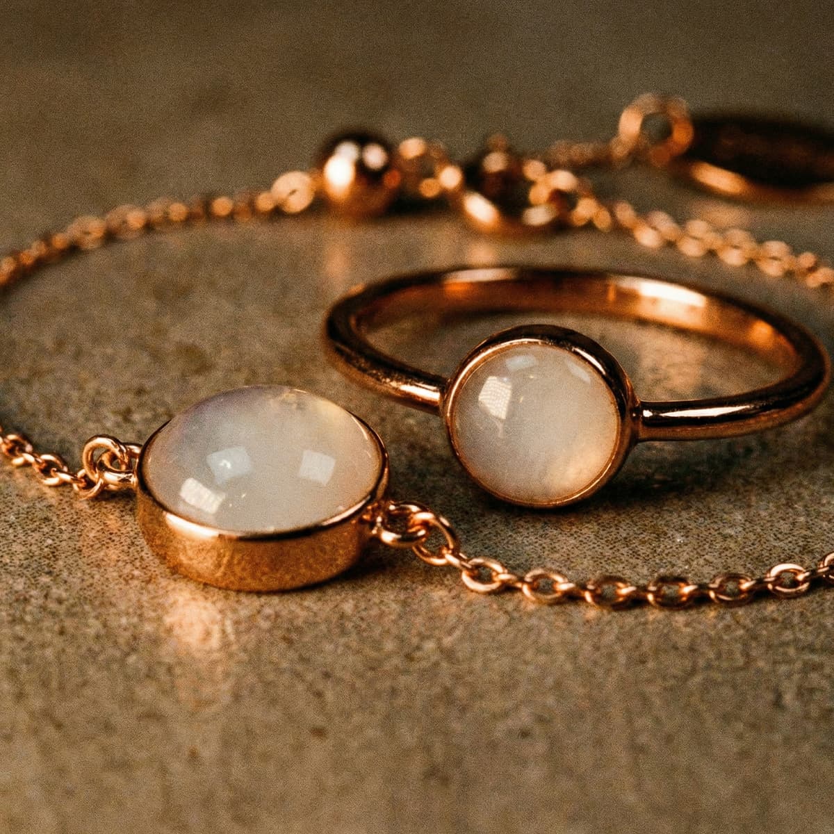 Gold chain jewelry set featuring a milky-white resin stone, including a diy breastmilk bracelet charm and matching ring displayed on a neutral textured background.