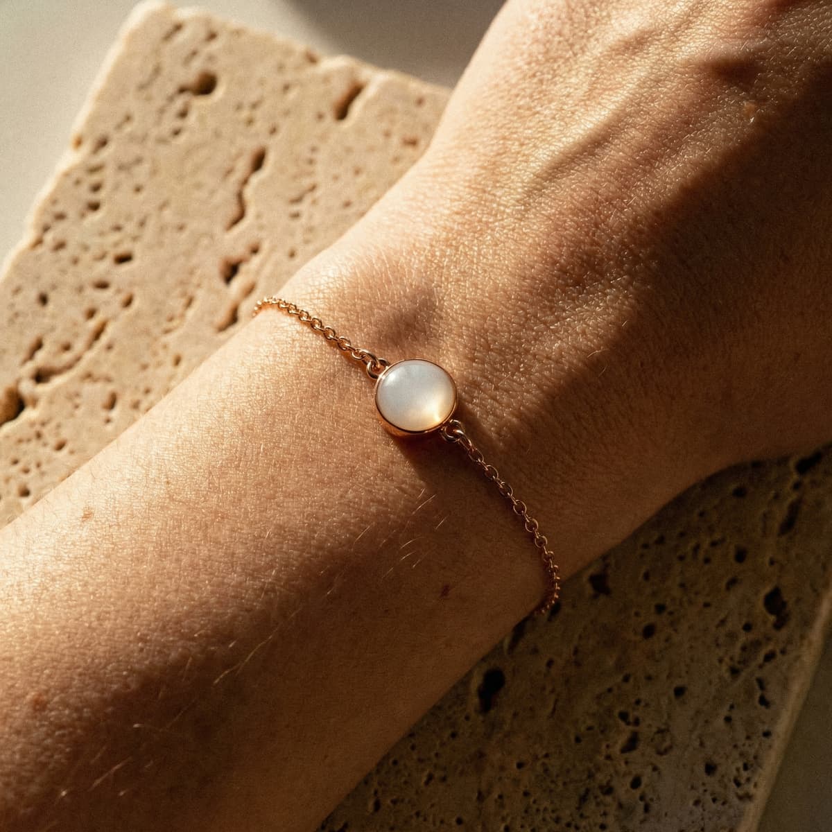 Close-up of a wrist wearing a minimalist rose-gold chain keepsake bracelet with a milky white resin stone, a delicate style often chosen for diy breastmilk bracelets in warm natural light.