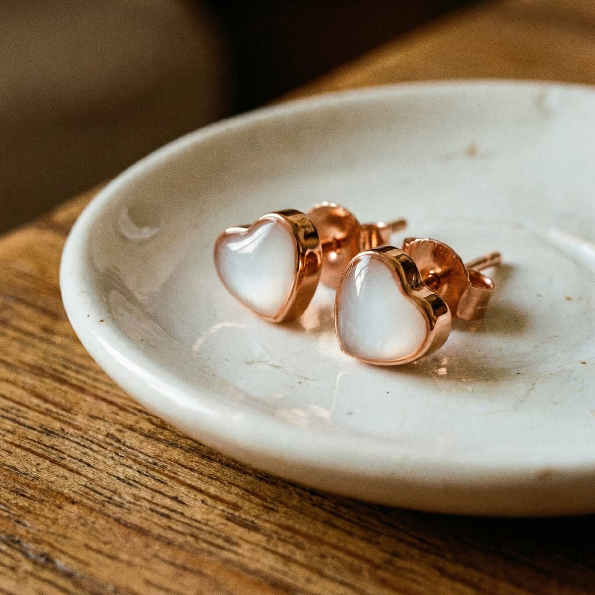 Rose-gold heart stud earrings with milky white resin centers, a diy breastmilk earring keepsake displayed on a ceramic dish.