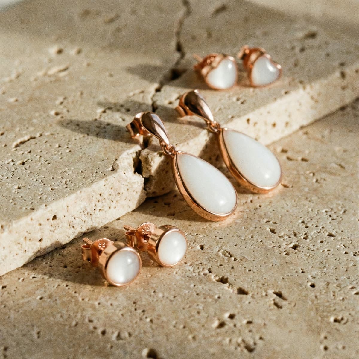 Rose gold drop and stud jewelry set with creamy white resin stones, showcasing a diy breastmilk earring keepsake design on a textured stone background