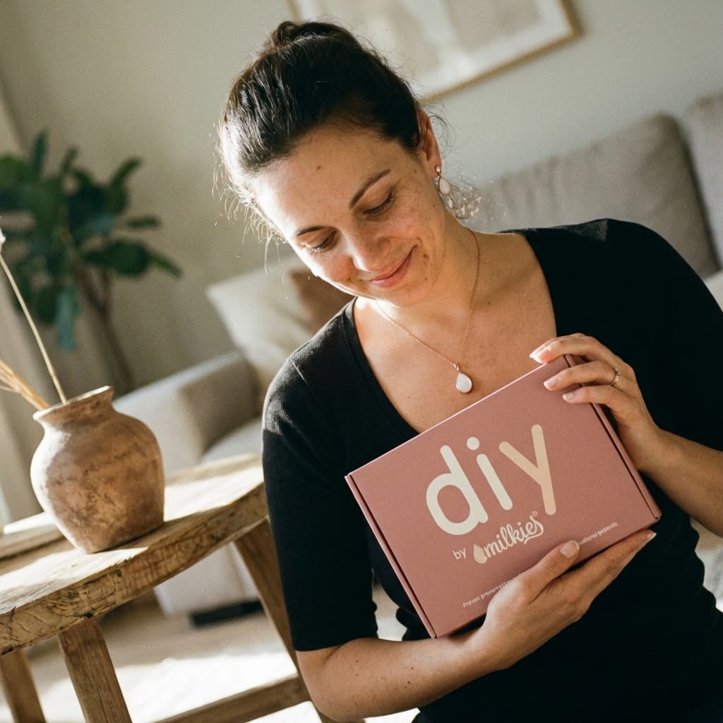 Smiling mother at home holding a pink DIY by MILKIES box, highlighting why a diy breastmilk jewellery kit is a convenient, private way to create your own keepsake.