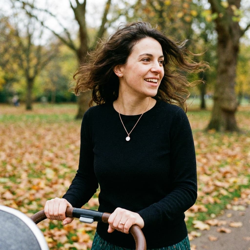 Mom smiling outdoors while pushing a stroller, wearing a delicate pendant necklace made with a diy breastmilk jewelry kit