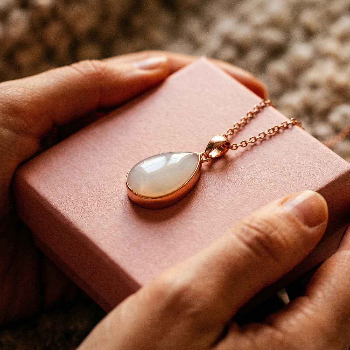 Hands hold a pink gift box featuring a rose-gold teardrop pendant, highlighting why a diy breastmilk necklace kit is a meaningful at-home way to create a personal keepsake.