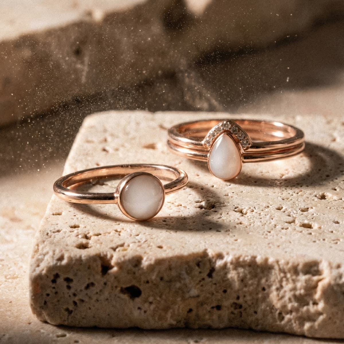 Rose-gold jewelry set on a textured stone surface featuring a diy breastmilk ring with a milky white resin stone, lit by warm light with fine dust in the air.