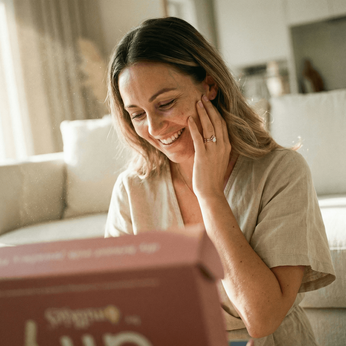 Smiling mother at home admiring her diy breastmilk rings beside the DIY by MILKIES kit box, showing why an easy, private at-home keepsake kit is a great choice.