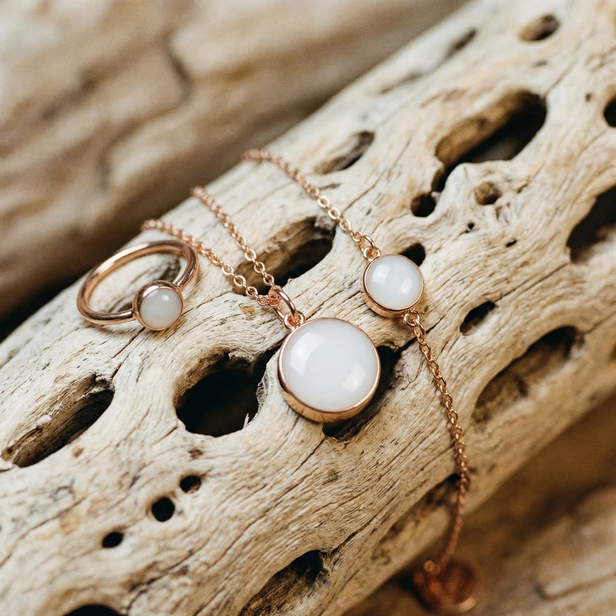 Rose gold breastmilk keepsake jewelry set with milky white resin stones (necklace, ring, bracelet) symbolizing a mother’s journey through drying up milk, displayed on natural driftwood.