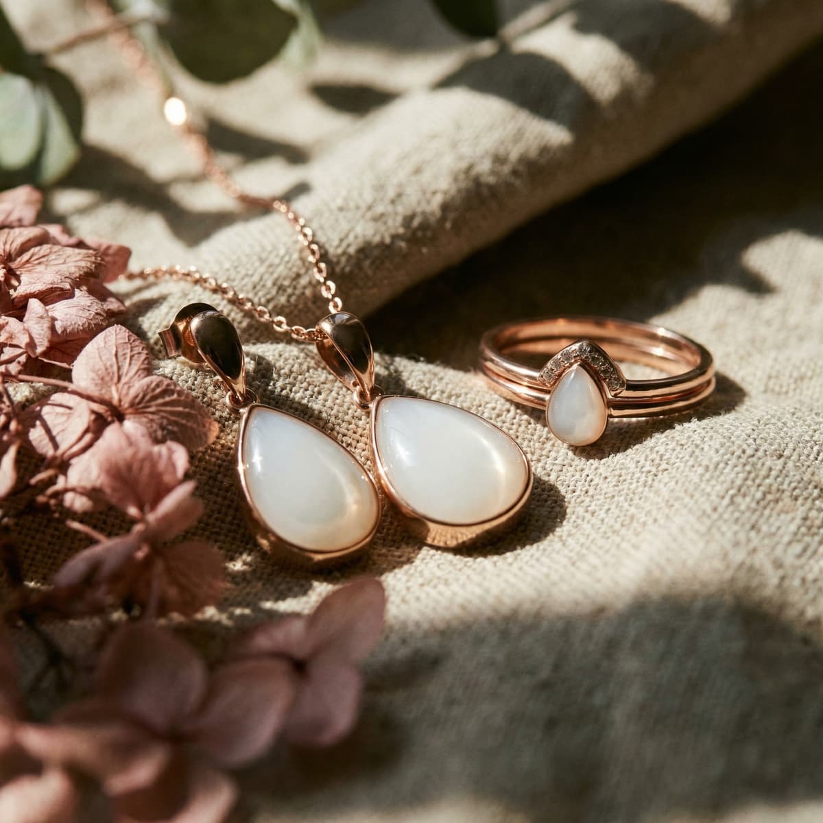 Rose-gold breastmilk keepsake jewelry set with teardrop earrings, necklace pendant, and stacked rings featuring milky resin stones, showing how mothers can preserve their milk in resin without drying up milk, styled on soft fabric with dried flowers.