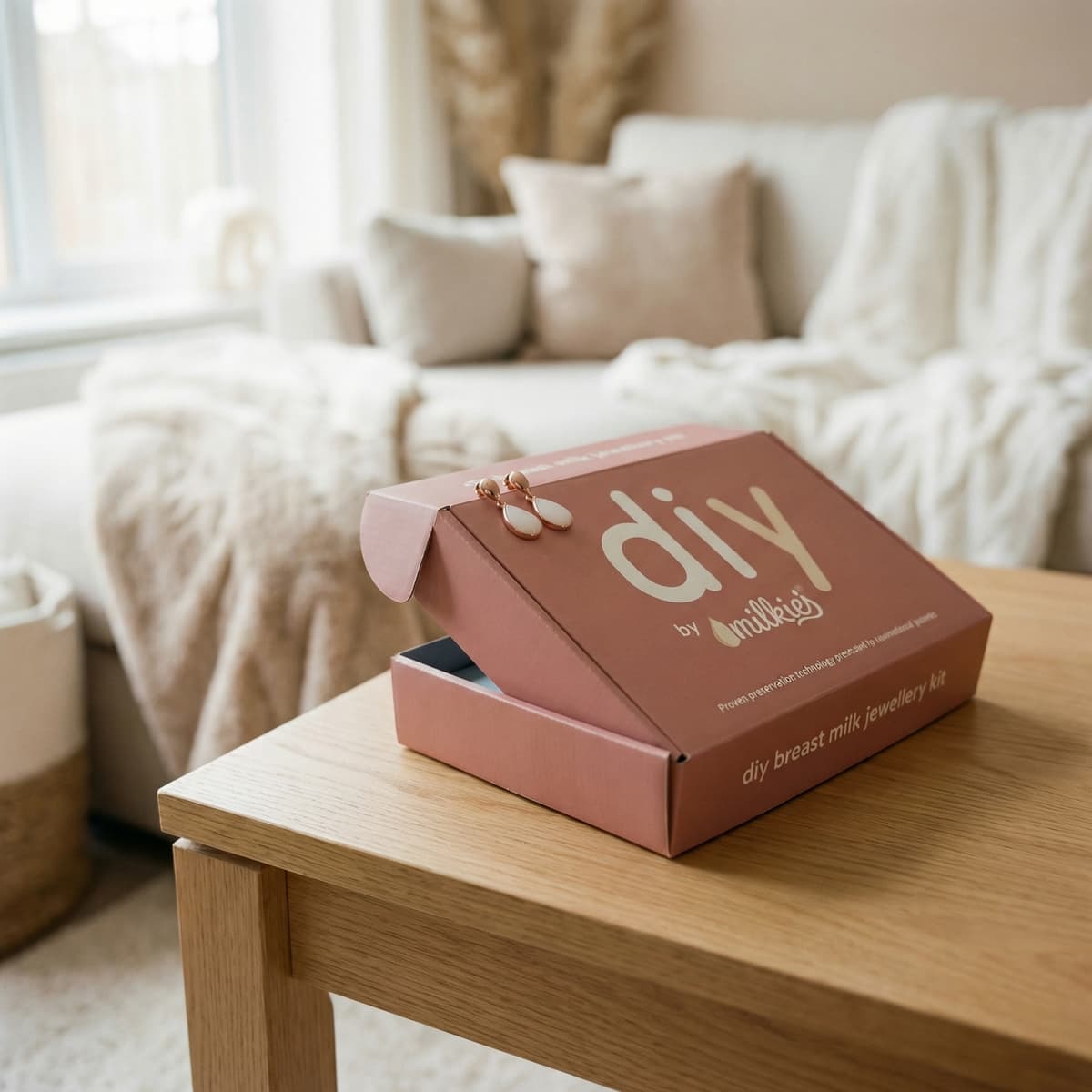 Open DIY by MILKIES breast milk jewellery kit box on a wooden table in a cozy living room, a thoughtful end of breastfeeding gift for creating a keepsake at home.
