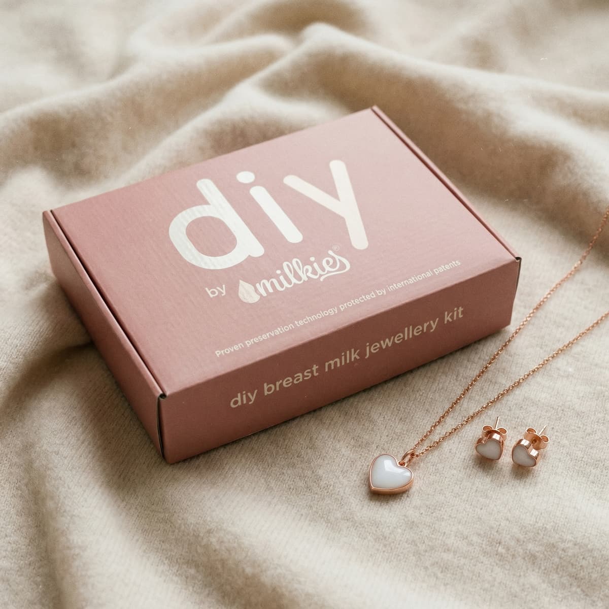 DIY by Milkies breast milk jewellery kit box with heart necklace and matching earrings displayed on soft fabric, a meaningful gift for new mother to create a keepsake at home
