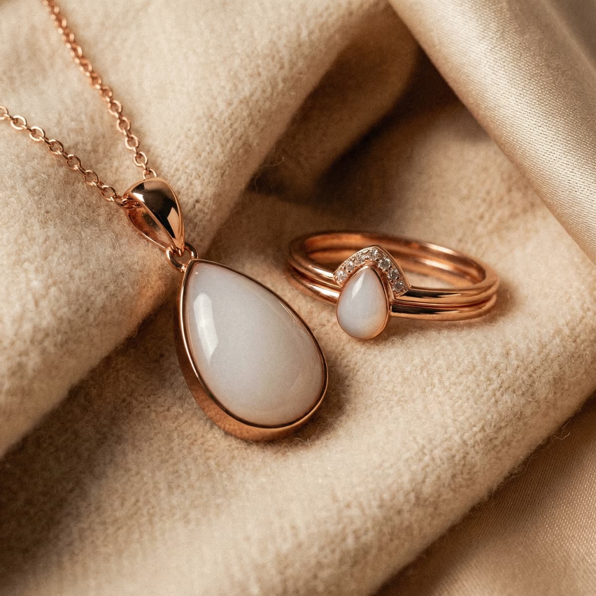 Rose-gold teardrop pendant necklace and matching ring with milky white resin stone, a last feed keepsake jewelry set displayed on soft beige fabric.