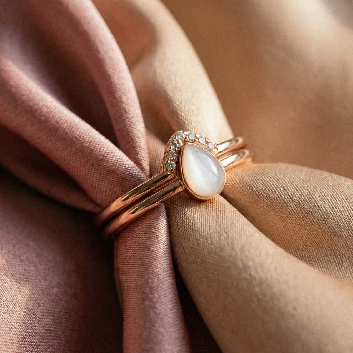 Rose gold teardrop ring featuring a milky white resin stone and small crystals on blush and beige fabric, an elegant motherhood keepsake jewelry piece.