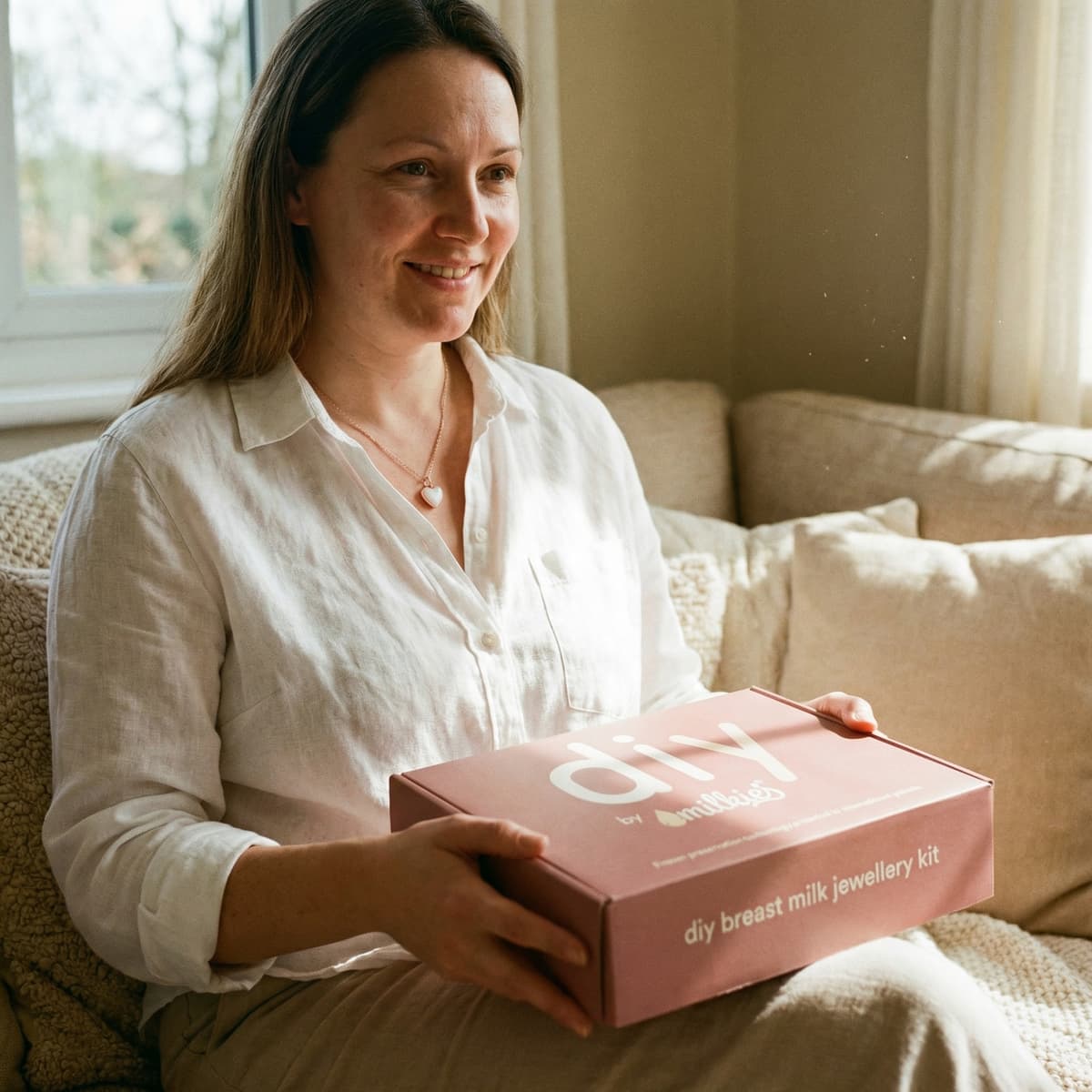 Smiling mom at home holding a DIY by MILKIES breast milk jewellery kit box, highlighting an easy, private way to create a meaningful motherhood keepsake.