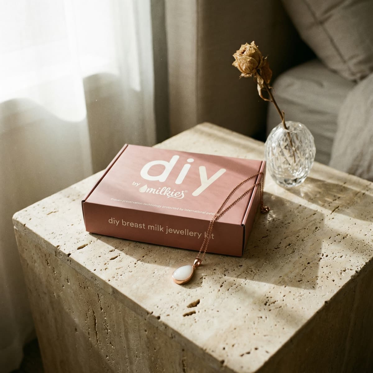 DIY by Milkies breast milk jewelry kit box with a rose-gold necklace on a stone table by a window, a meaningful push present keepsake for new moms