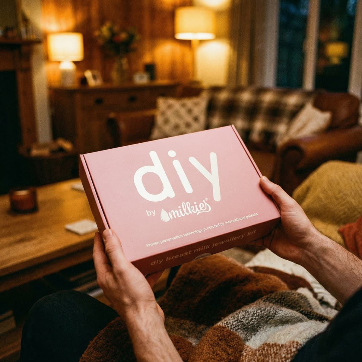 Cozy living room scene showing someone holding a DIY by MILKIES breast milk jewellery kit box, a thoughtful push present for wife to create a keepsake at home.