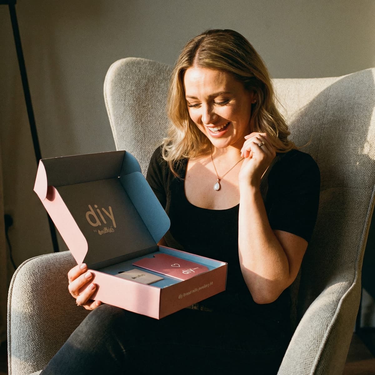 Smiling new mom opening a DIY by MILKIES breastmilk jewelry keepsake kit at home, a meaningful option among push present ideas for creating a personal at-home breastmilk keepsake.