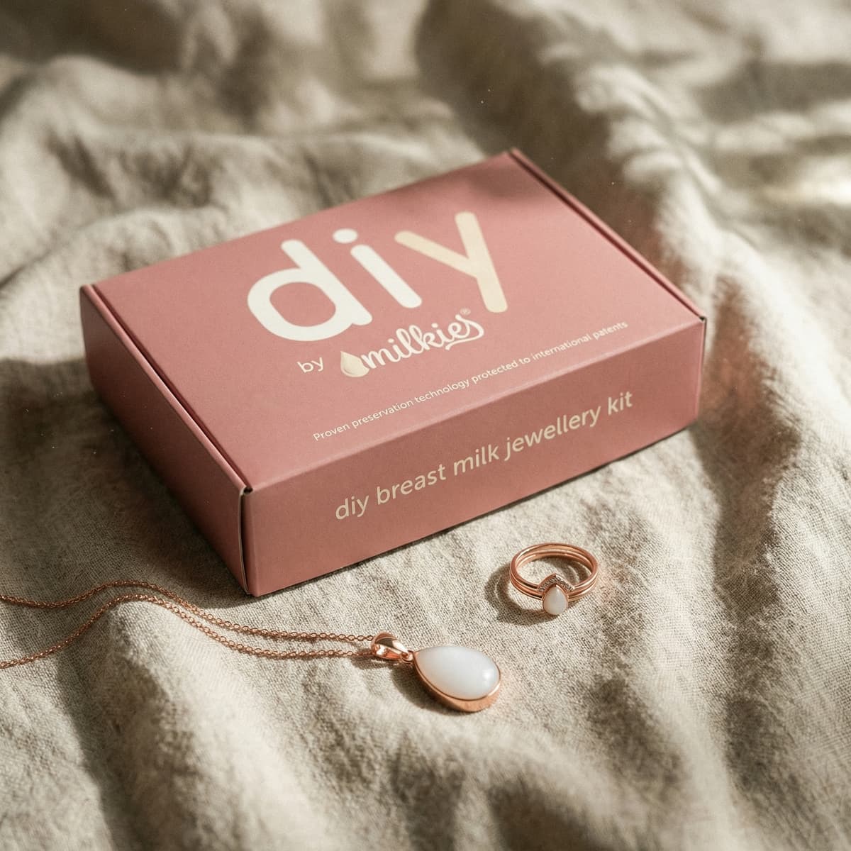 Pink DIY by MILKIES breast milk jewellery kit box with rose-gold necklace pendant and matching ring on soft fabric, offering unique push present ideas for new moms