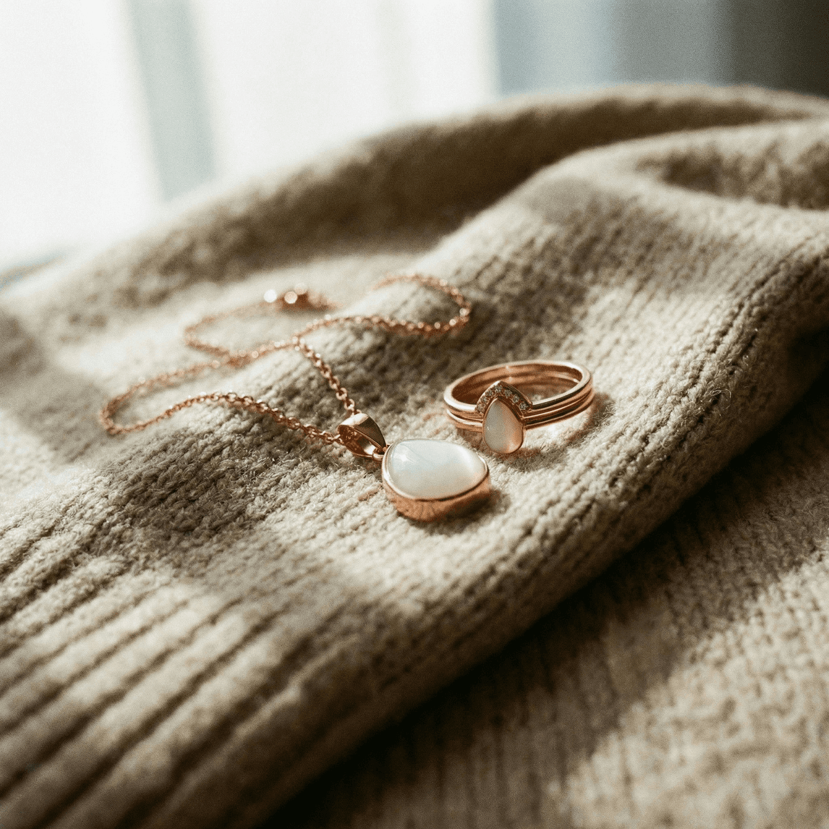 Rose-gold breastmilk keepsake necklace and ring with milky-white stones on a beige knit sweater, a meaningful memento for moms stopping breastfeeding.