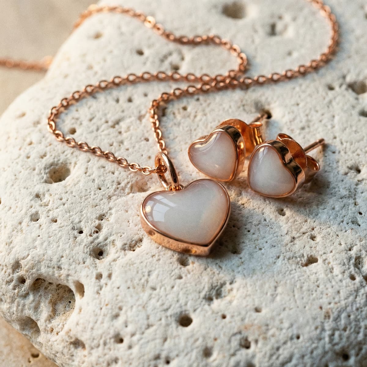 Rose gold heart pendant necklace and matching heart stud earrings on a textured stone surface, elegant jewelry set perfect for unique push presents